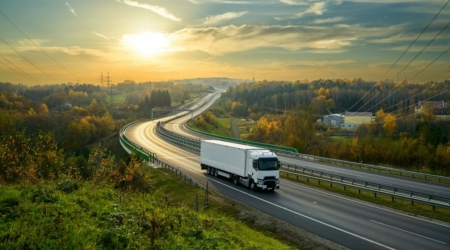 White truck driving on the highway winding through forested landscape in autumn colors at sunset